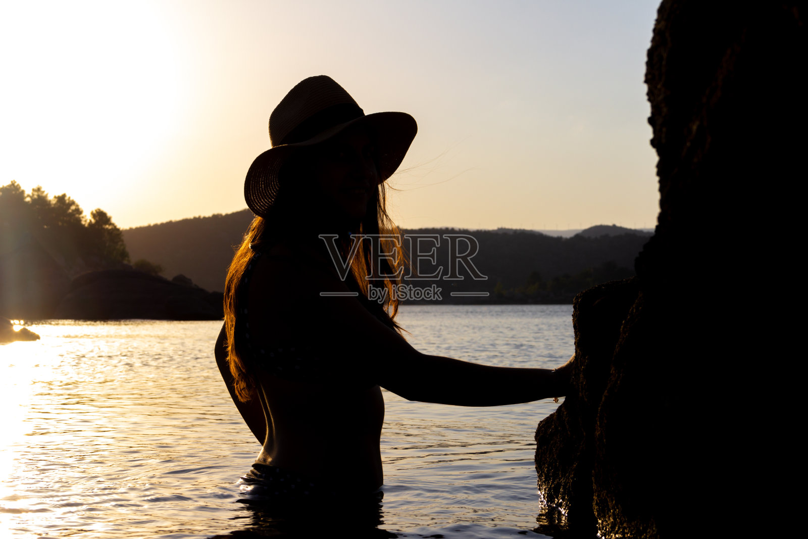 一个穿比基尼的女人，半边身子在夕阳下的湖水里。有选择性的重点。照片摄影图片