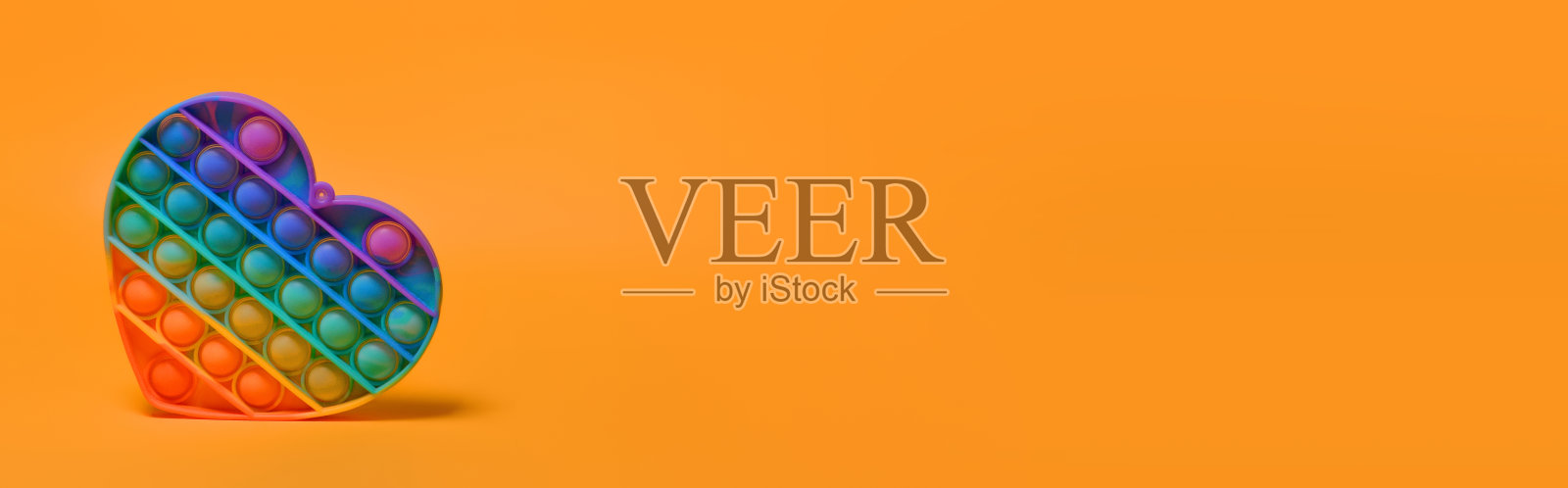 流行它-新的流行的彩色硅胶感官时尚玩具抗压力的形式在一个橙色的背景上的心。彩虹的颜色。副本的空间。横幅照片摄影图片