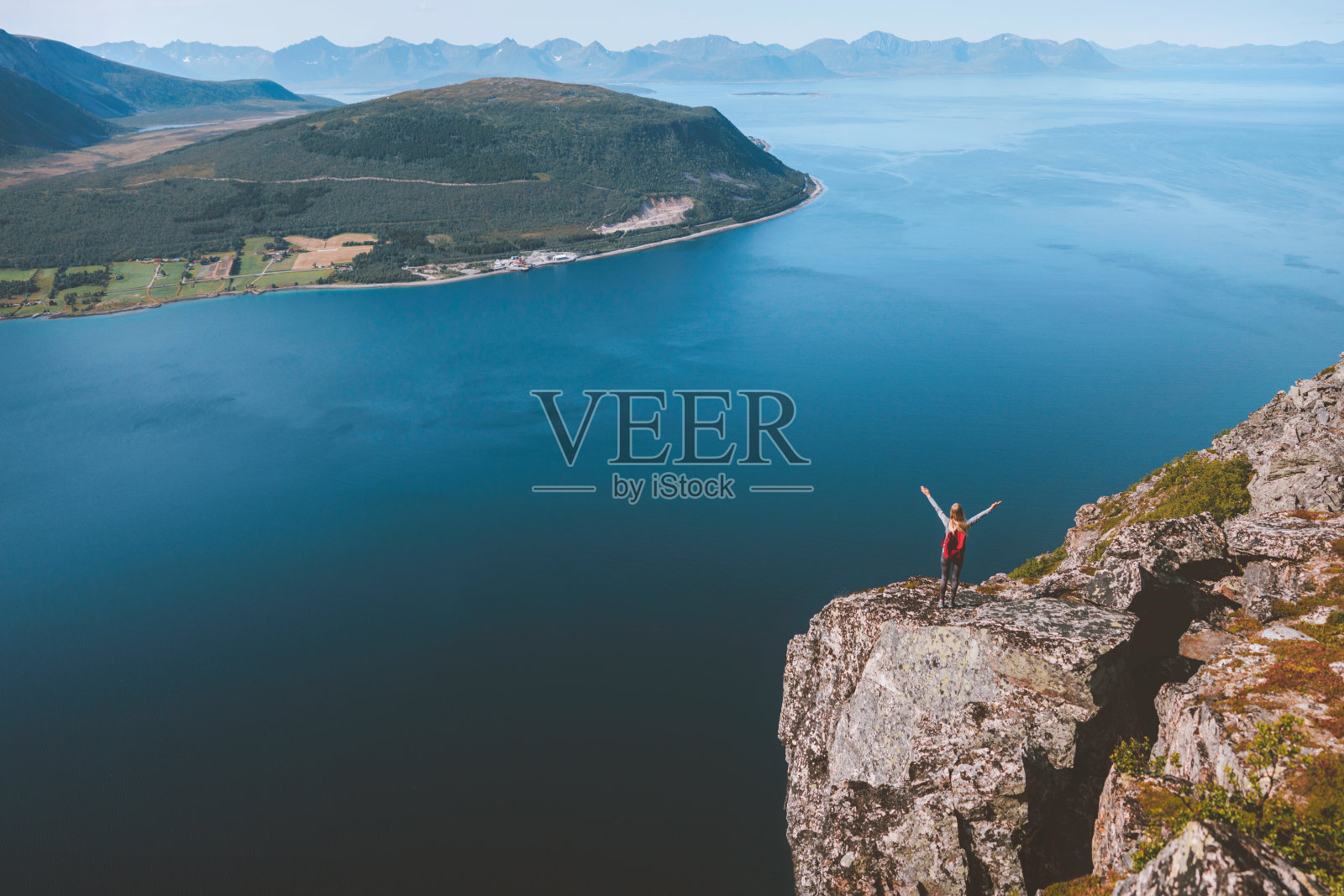 旅行者举起手，独自站在悬崖边，看着挪威的空中海景，独自徒步旅行，户外活动，健康的生活方式照片摄影图片