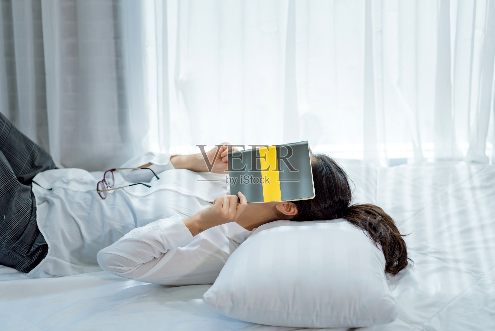 年轻的亚洲妇女在家里的床上看书后感到困倦。照片摄影图片