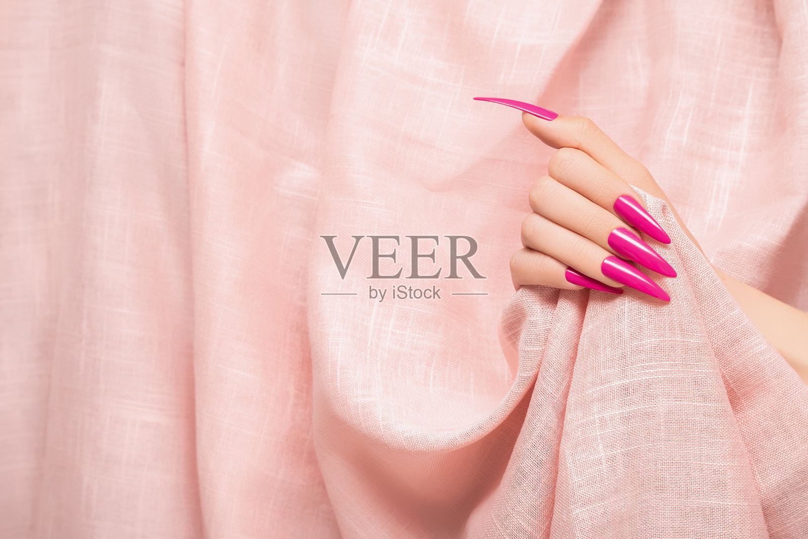 女性手与粉红色细高跟鞋指甲设计。长指甲修指甲。女人手放在浅粉色织物背景上照片摄影图片