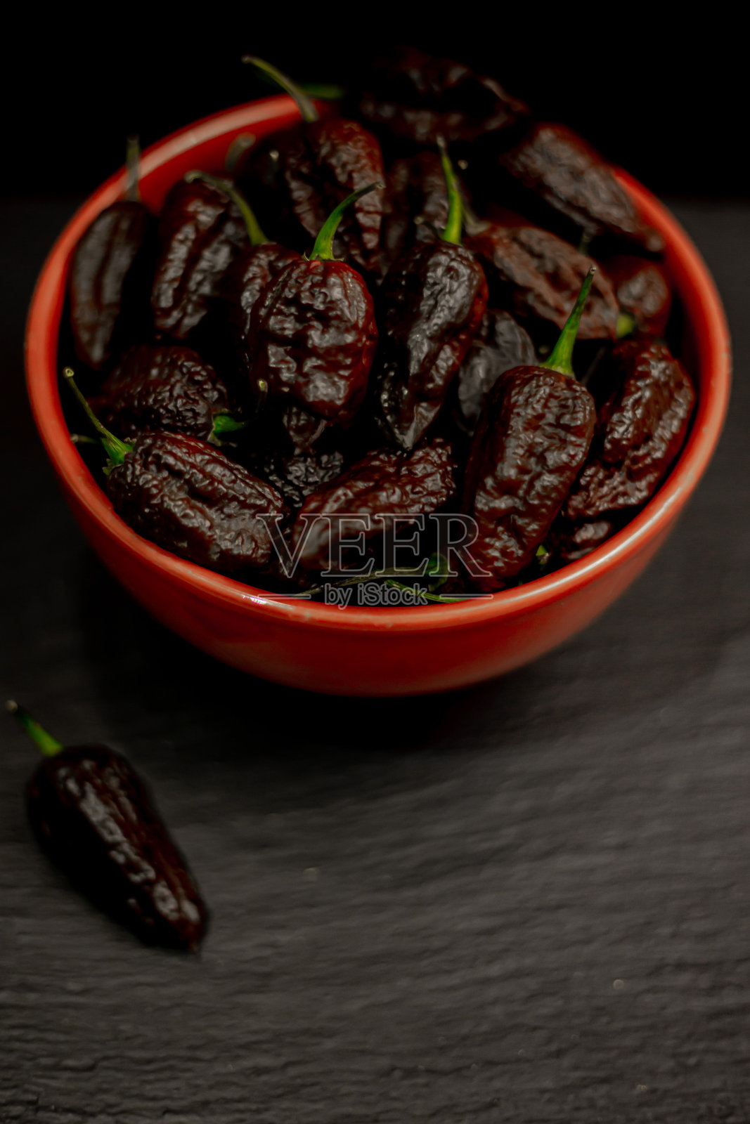 一碗超辣辣椒七锅疯狂巧克力，哈瓦那辣椒，鬼椒，黑色桌子上的超辣辣椒照片摄影图片