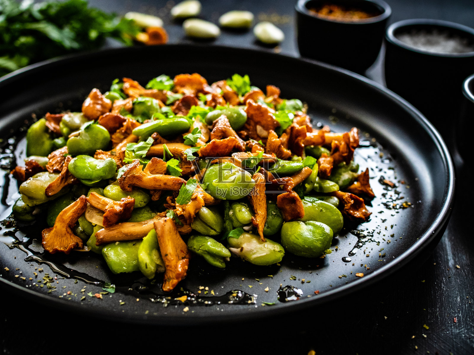 木桌上放着炸鸡油菌、大蒜和欧芹的蚕豆沙拉照片摄影图片