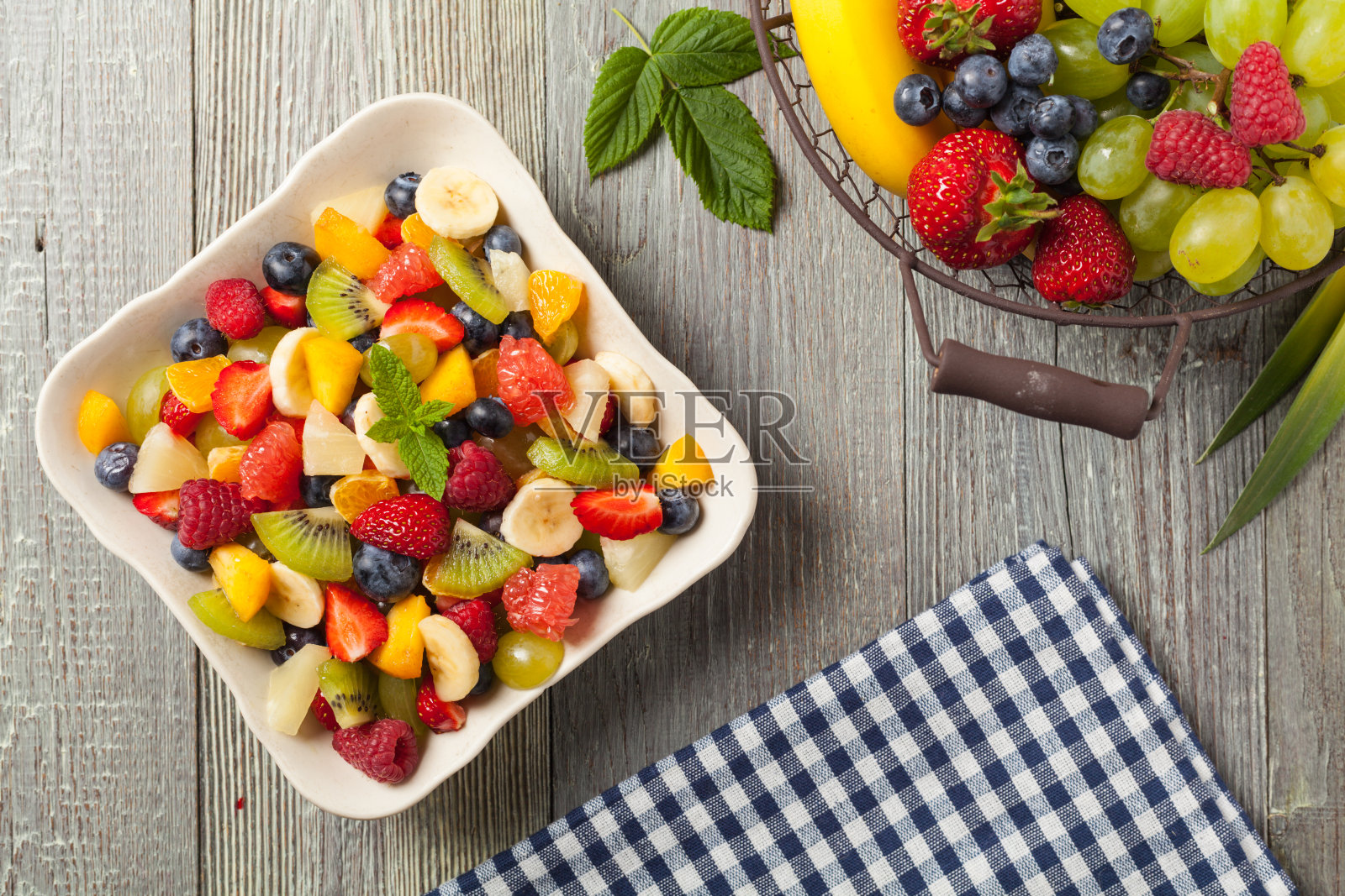 美味的水果沙拉与新鲜的水果。背景是木制的灰色桌子。照片摄影图片