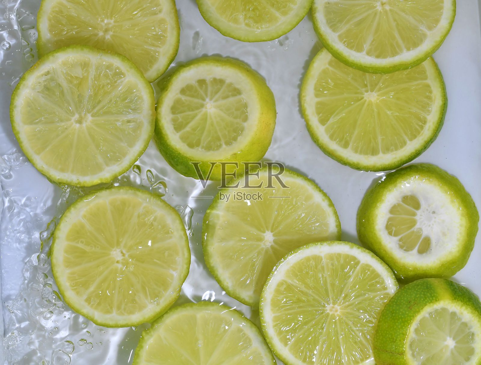 白色背景上的水里的酸橙片。近距离观察气泡液体中的酸橙。将成熟的黄色酸橙片放入水中。水果在水中的宏观图像照片摄影图片