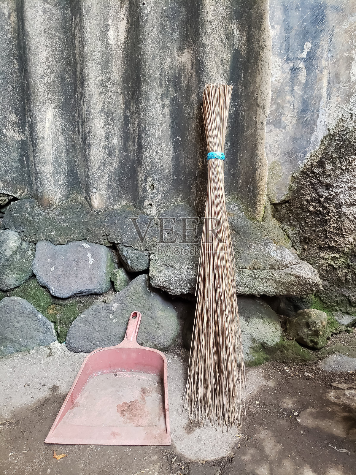 把扫帚杆和塑料簸箕合起来，靠着一堵石墙扫院子照片摄影图片