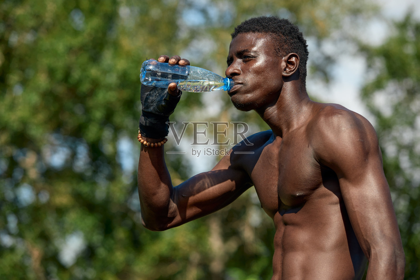 年轻的非洲裔美国人一边喝水一边在公园操场上训练，户外运动的概念照片摄影图片
