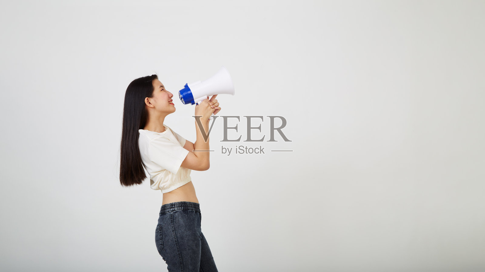 微笑开朗的年轻漂亮的亚洲女人手持扩音器在孤立的演播室宣布照片摄影图片