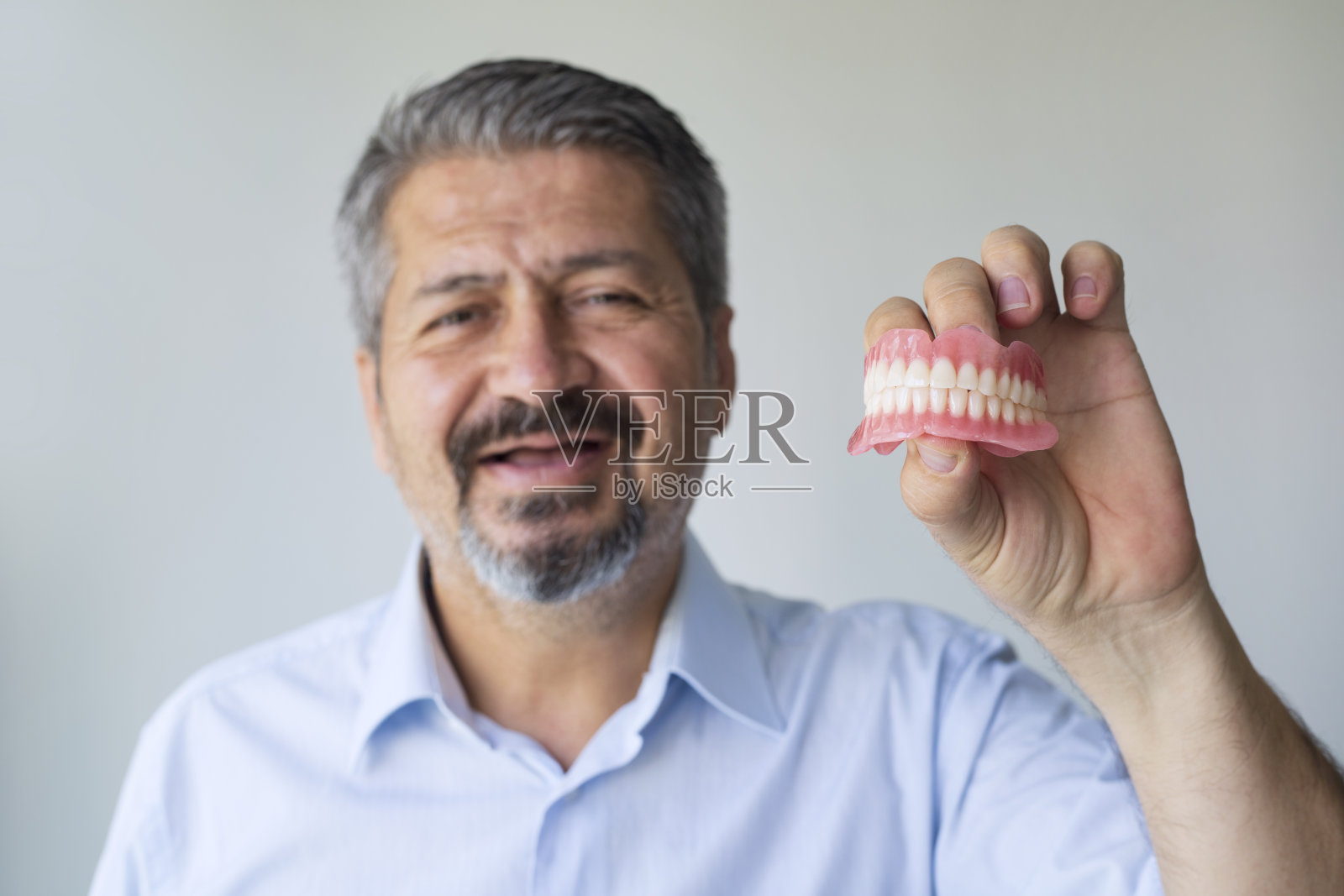 一位头发花白的老人托着他的假牙。男人戴上假牙。植体。正畸治疗。老的年龄。牙齿。下巴。广告。关闭计划。从以上观点。义齿。照片摄影图片