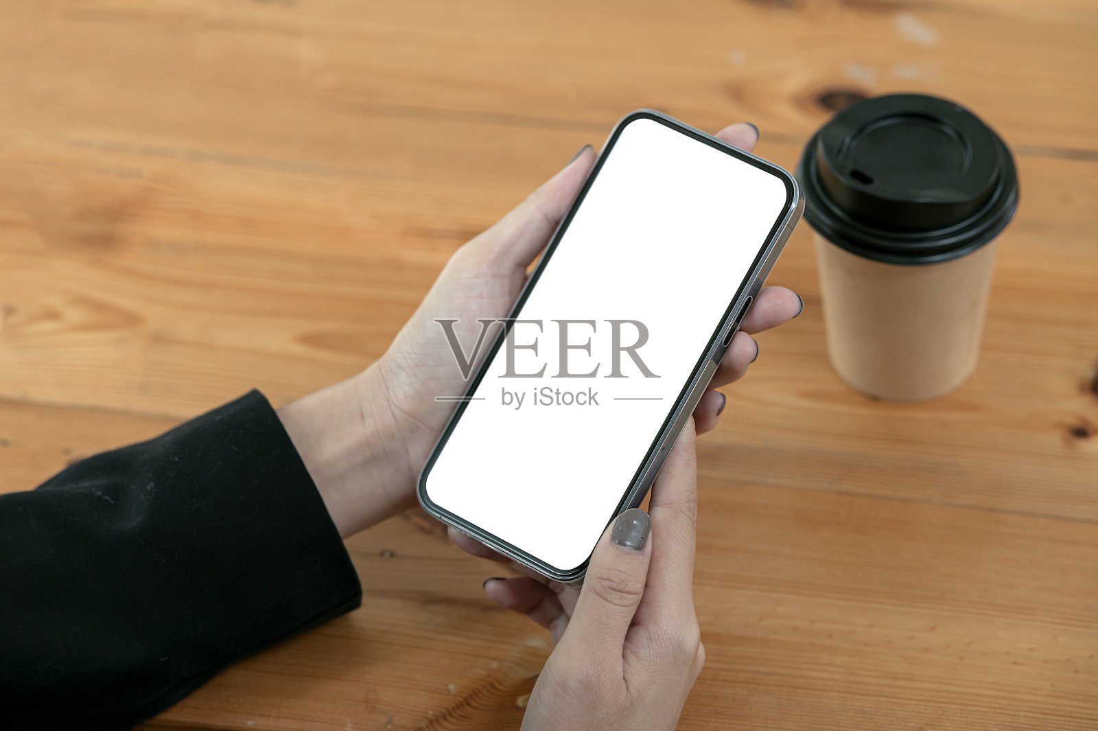 一名女子坐在桌边，手拿空白屏幕的智能手机。照片摄影图片