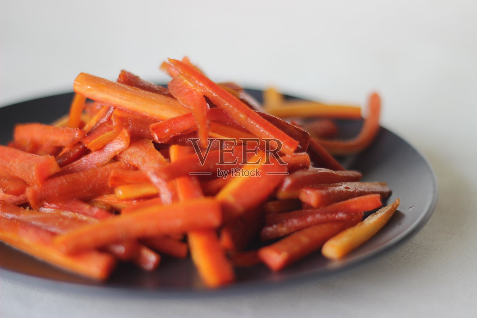 焦糖胡萝卜条。用黄油和糖炒的胡萝卜。又快又健康的零食。照片摄影图片