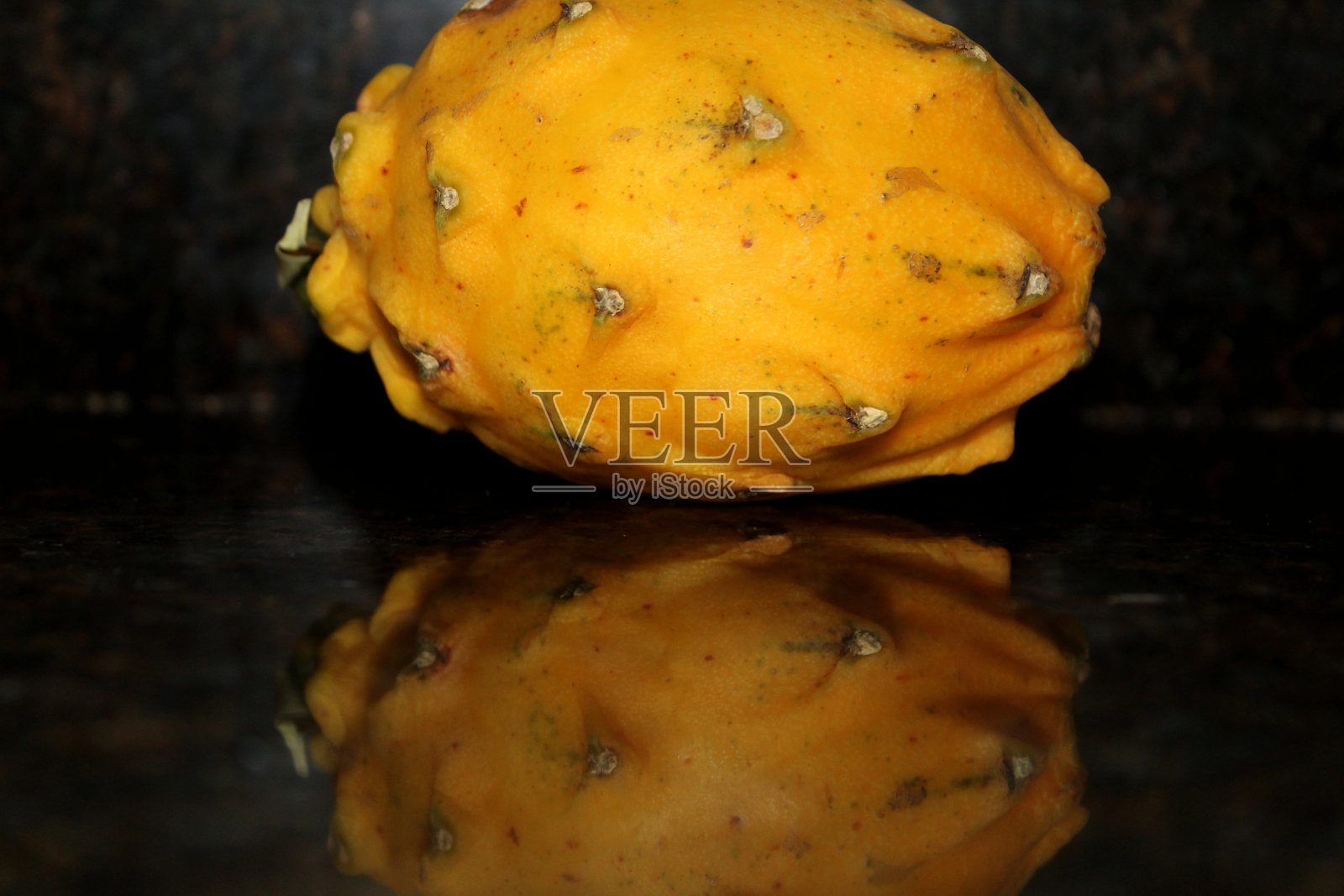 黄色的火龙果和它在黑色大理石台面上的倒影照片摄影图片