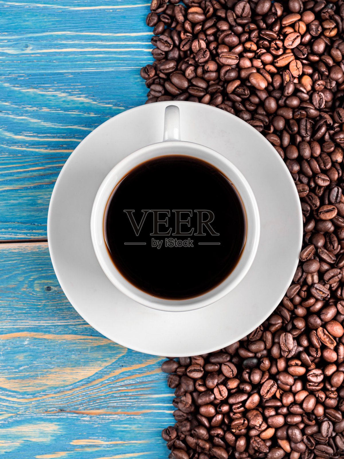 蓝色木桌上放着蓝色杯子里的黑咖啡，周围是咖啡豆照片摄影图片