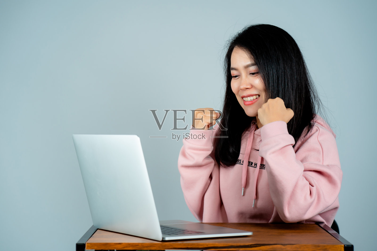 一个穿着粉红色衬衫的亚洲女孩的肖像。坐在笔记本电脑网上购物与一个快乐的脸背后的灰色工作室背景照片摄影图片