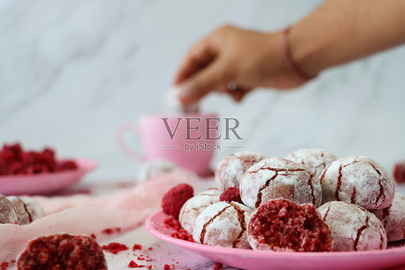 不认识的人浸泡个人的形象，新鲜烘焙的覆盆子杏仁饼干在粉红色的咖啡杯，旁边是一盘饼干，大理石效果的背景，聚焦前景照片摄影图片