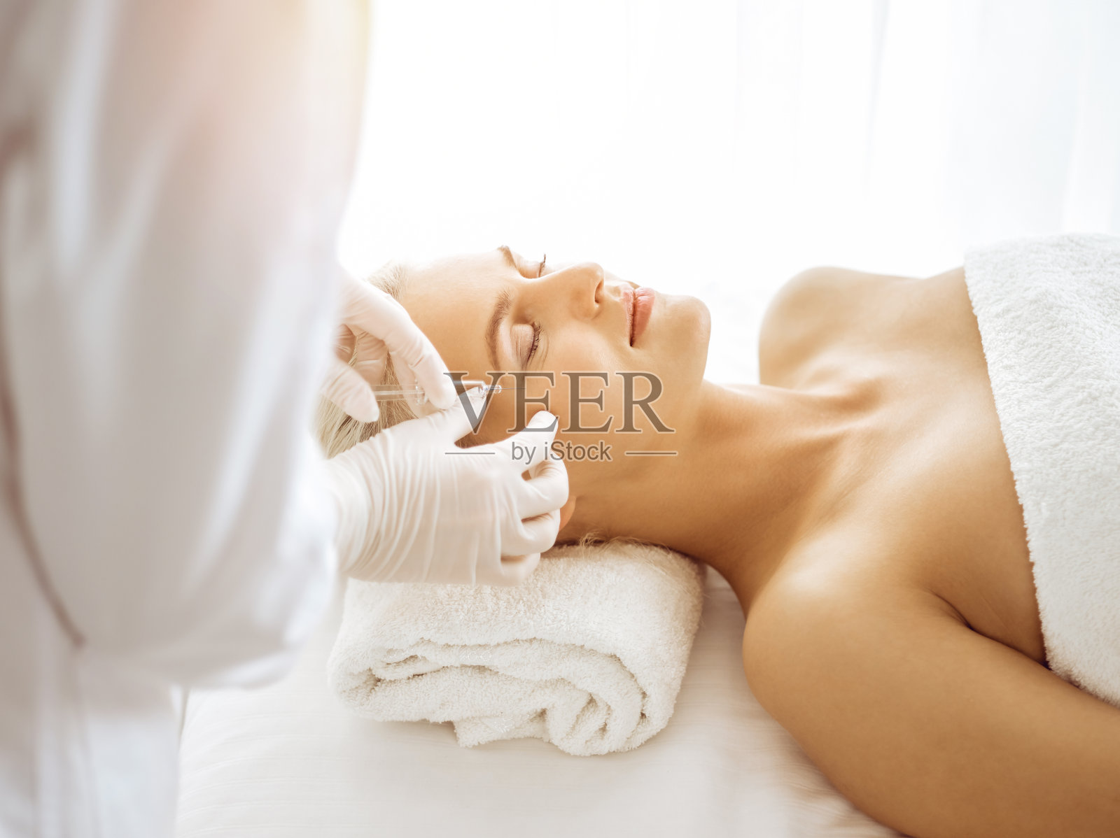 在阳光诊所，美容师正在用注射器给女性面部做美容手术。美容医学与外科手术，美容注射概念照片摄影图片