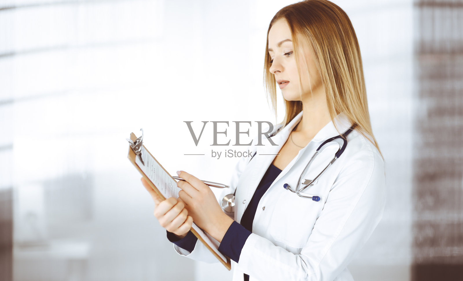 一位年轻的女医生站在诊所的橱柜里，用写字板做着笔记。美丽的女医生和听诊器的肖像。医院完善的医疗服务医学的概念照片摄影图片