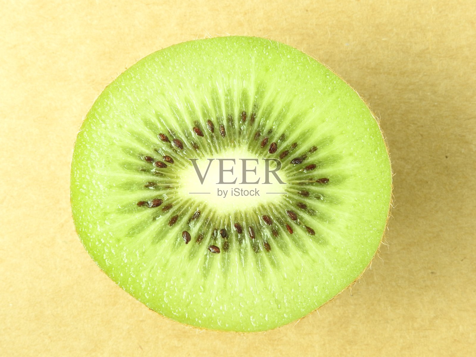 顶部视图和关闭成熟的新鲜猕猴桃切片棕色图案背景。猕猴桃有纤维状的绿色果肉和可食用的黑色种子。照片摄影图片