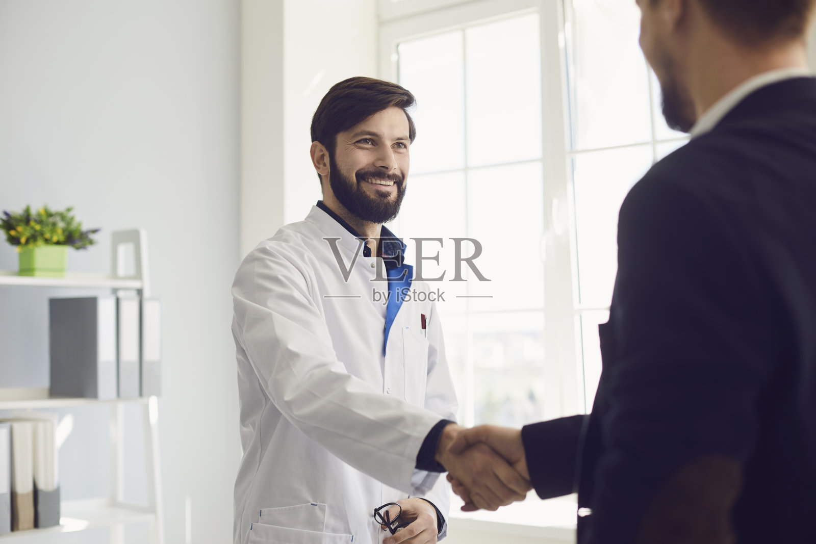 握手。在诊所里，执业医生和病人微笑着握手。照片摄影图片