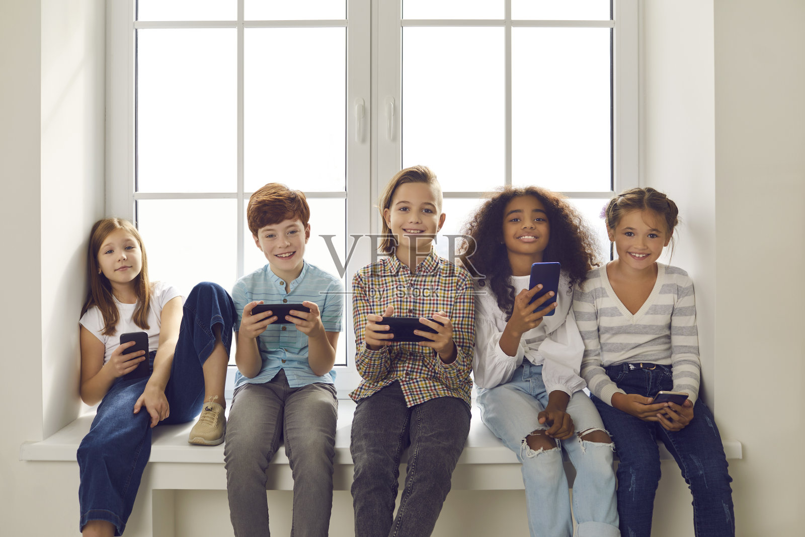 快乐的多民族儿童坐在窗台上玩手机游戏照片摄影图片