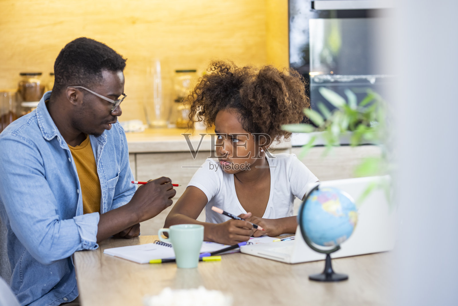 父亲和女儿坐在家里的桌子旁，试图做一些困难的家庭作业。照片摄影图片