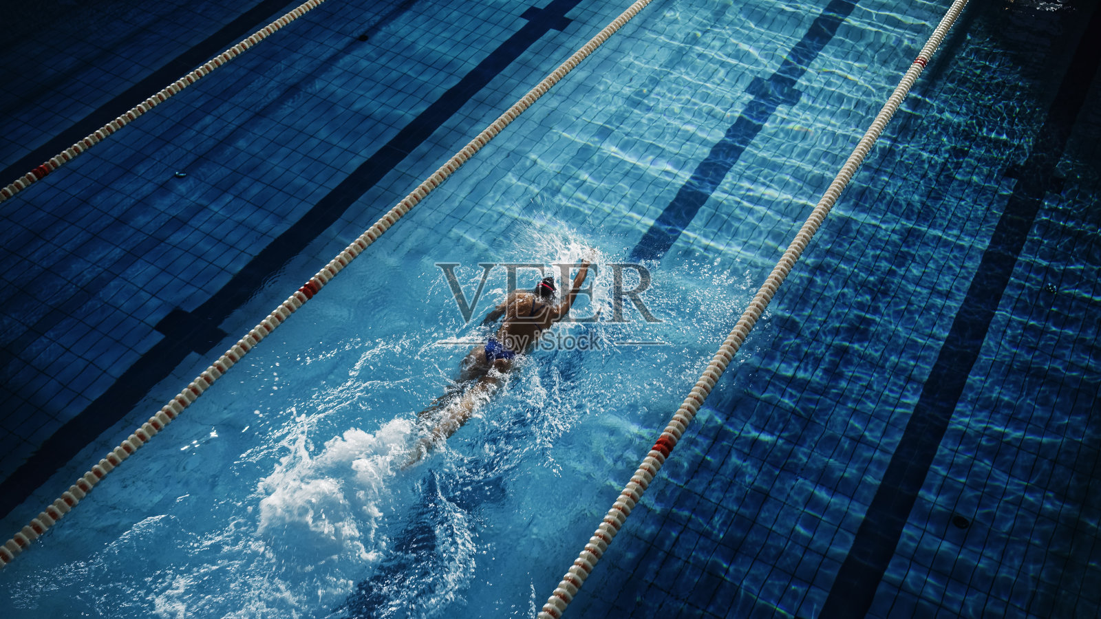 女子游泳选手在游泳池比赛。职业运动员克服压力和困难在黑暗戏剧性游泳池，电影圈灯显示良好的方式。空中拍摄照片摄影图片
