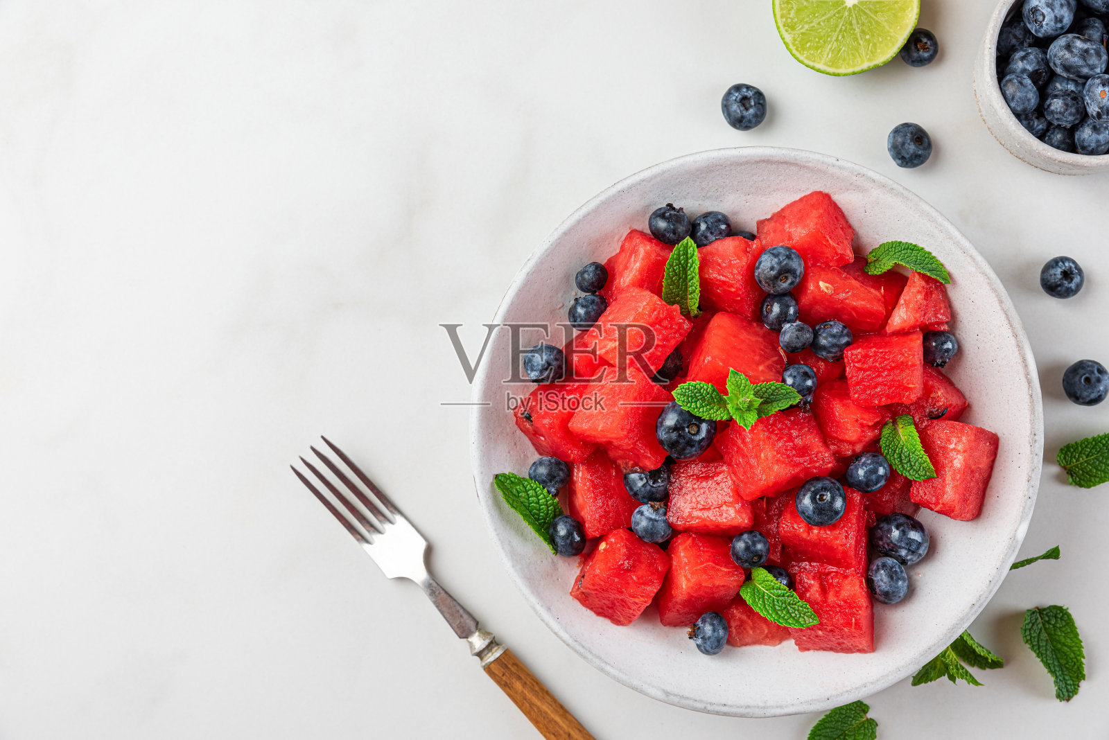 新鲜的夏季西瓜和蓝莓沙拉，配上薄荷和酸橙汁，放在白色背景的盘子里。俯视图照片摄影图片