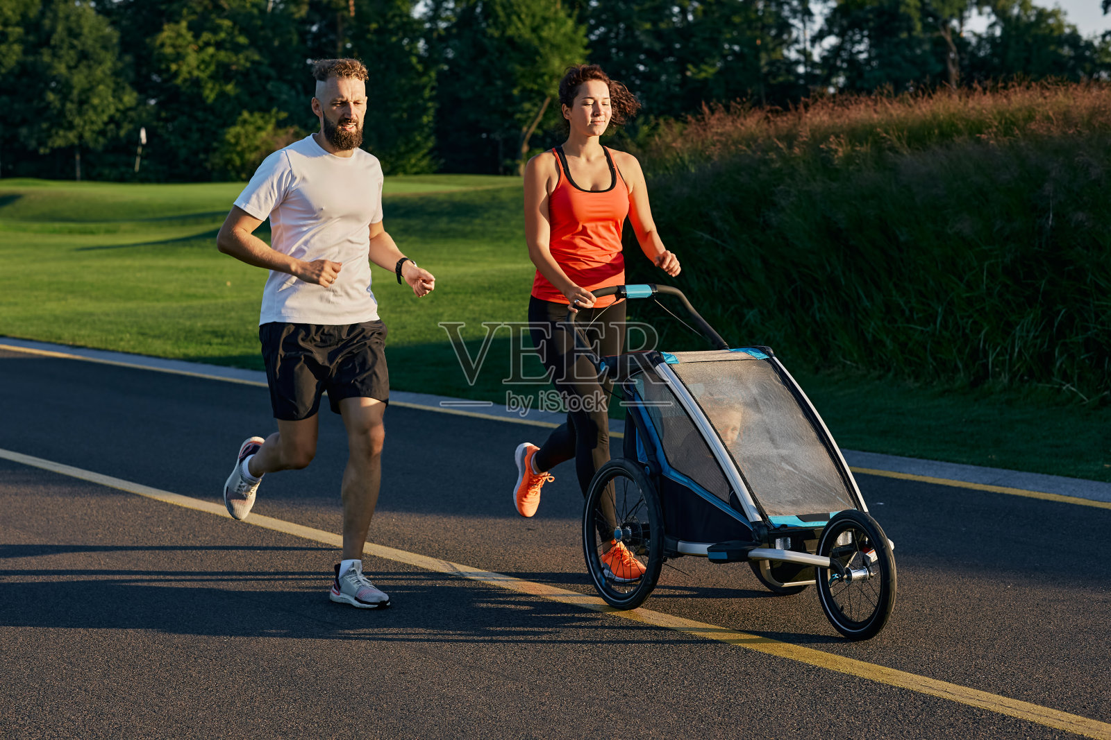 积极的家庭。年轻的家庭和他们的孩子在慢跑婴儿车在公园慢跑照片摄影图片