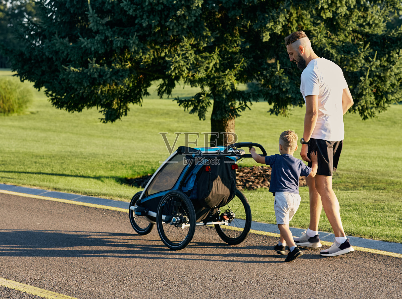 父亲和他的小儿子一起推着婴儿车在城市公园里散步。父亲，父亲和孩子。父亲节照片摄影图片