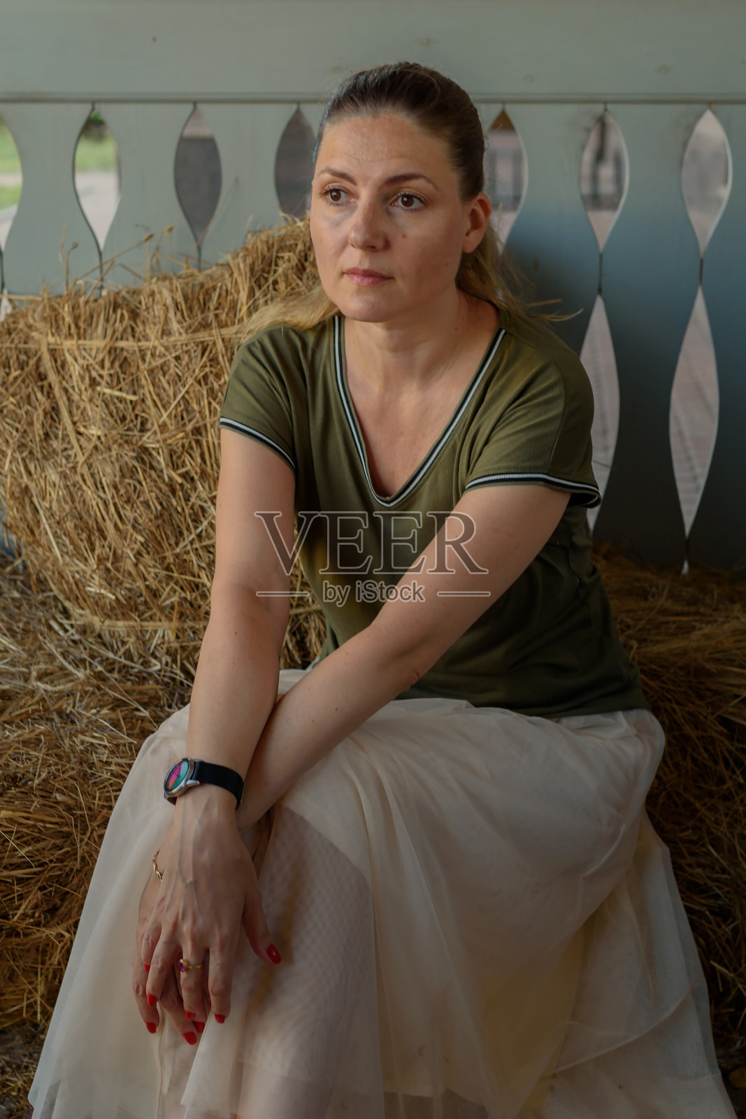 夏日里，一位长发飘逸的年轻女子，身穿长裙和t恤，坐在一家生态咖啡馆的稻草上。自然乡村背景下的女人肖像。生态旅游的概念照片摄影图片