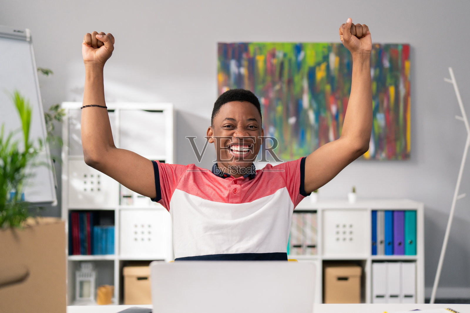 快乐的黑皮肤英俊的年轻员工坐在办公椅前的电脑，举起手，胜利，胜利，快乐，微笑，晋升，流动的钱，彩票，招标，合同照片摄影图片