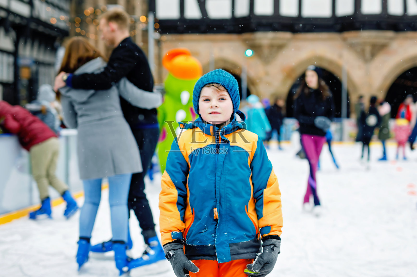 快乐的小男孩穿着五颜六色的暖和的衣服在圣诞市场或集市的溜冰场上滑冰。健康的孩子在滑冰中玩耍。许多人庆祝节日，有活跃的冬季休闲照片摄影图片