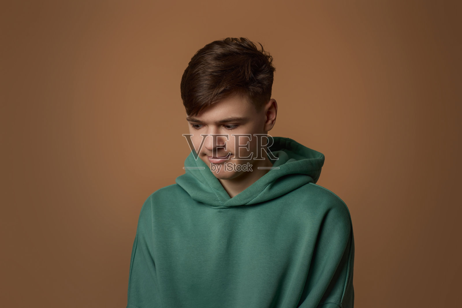 棕色背景下穿着运动衫的不高兴的年轻人照片摄影图片