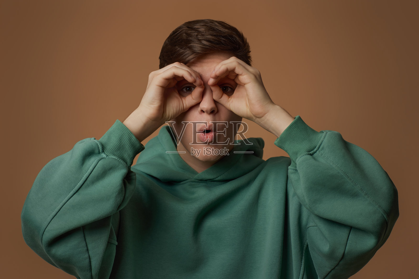 年轻人双手捂着眼睛，好像在用望远镜看照片摄影图片