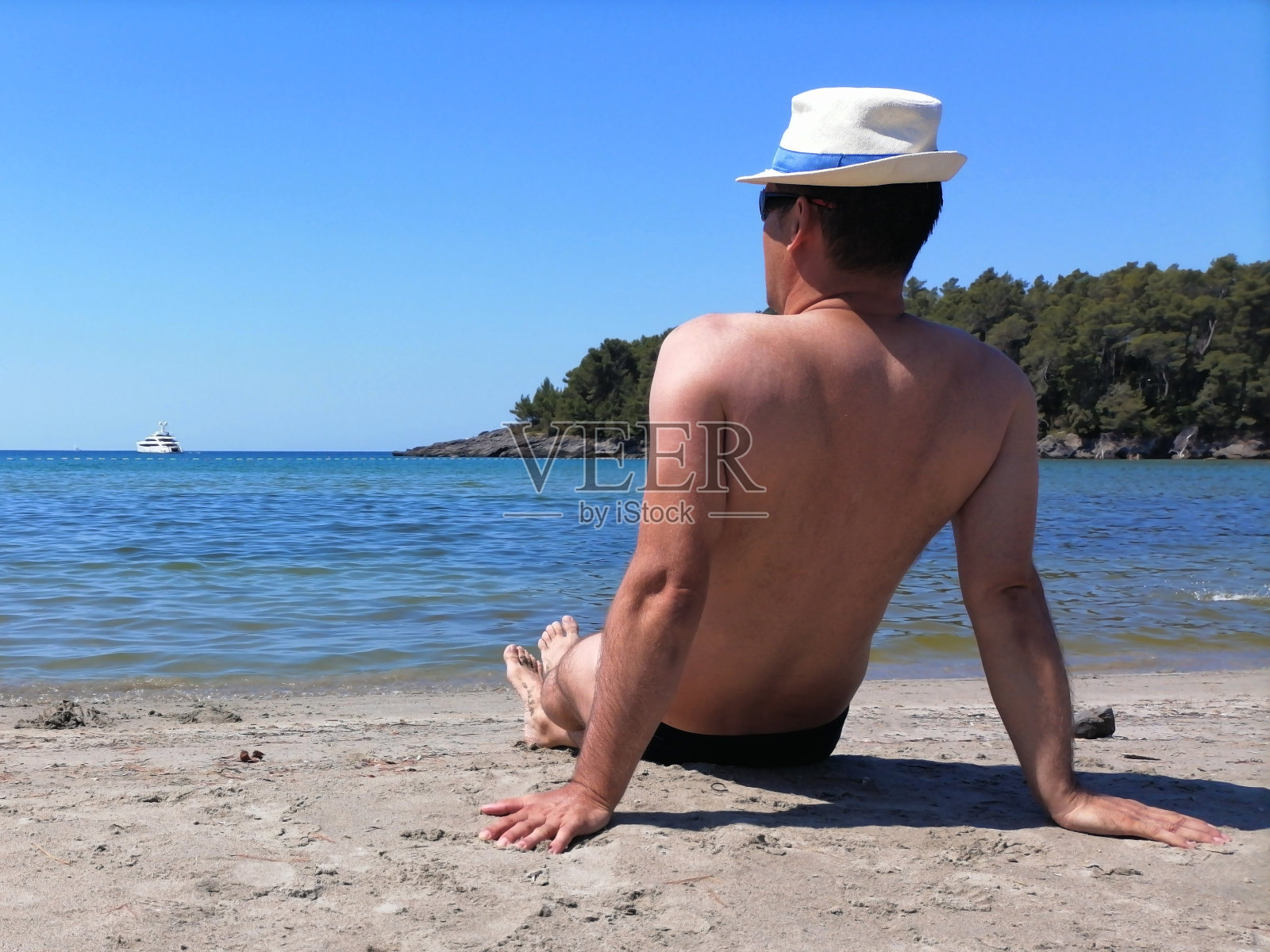 一个人坐在岸边看着大海。风景、森林、大海、游艇、蓝天。照片摄影图片