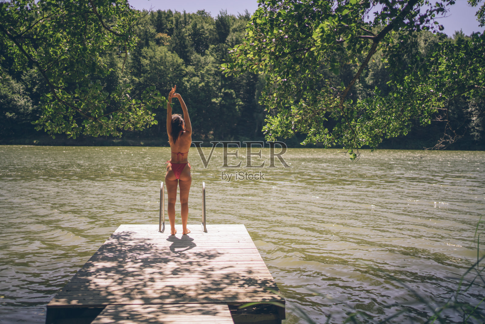 夏天，一个年轻女子在湖边的码头上休息照片摄影图片