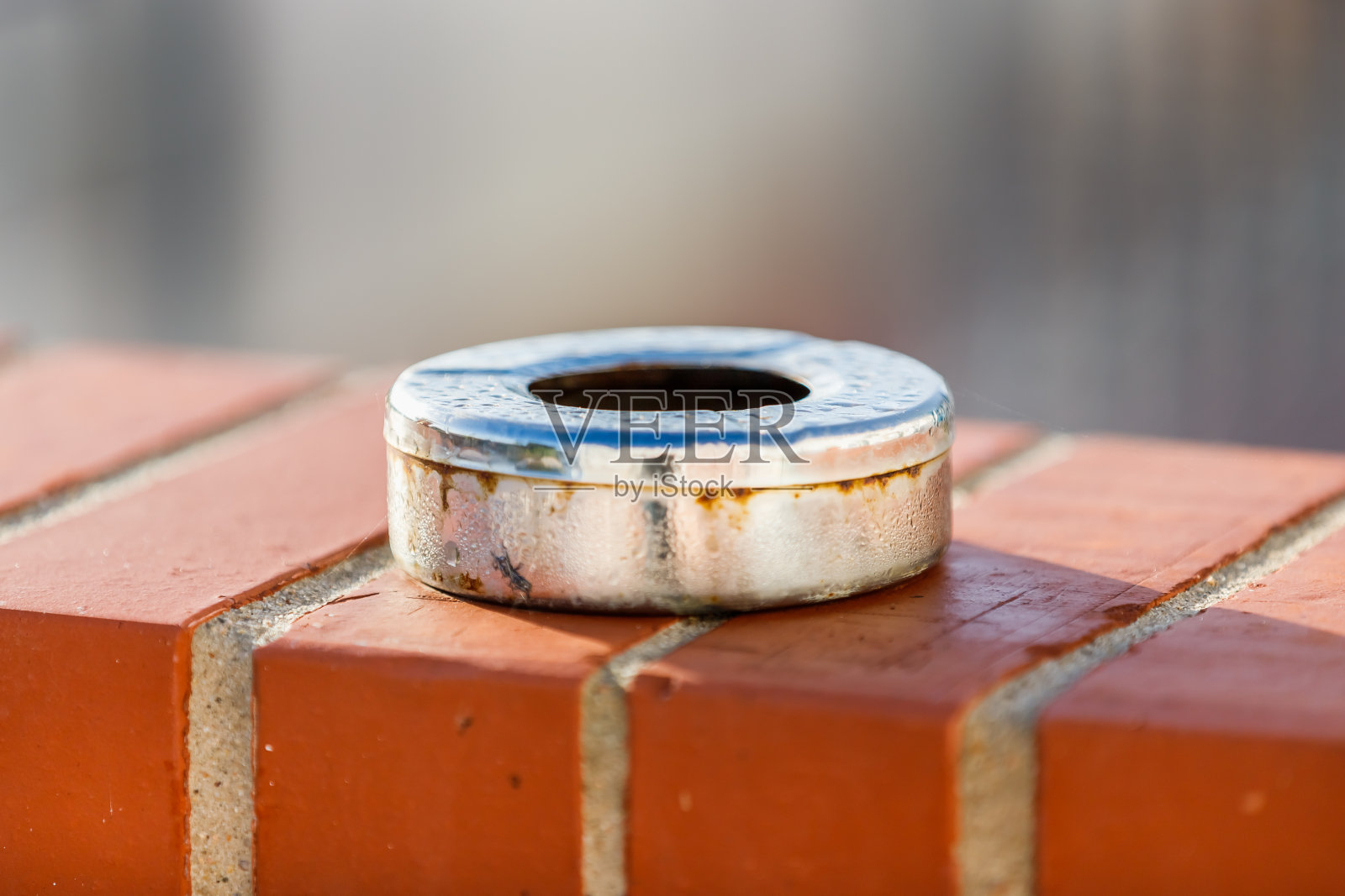 红色砖墙上的金属烟灰缸上挂着朝露照片摄影图片