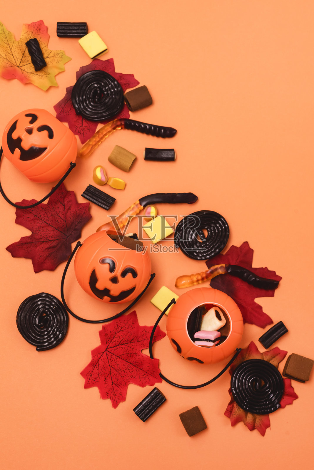 万圣节背景万圣节糖果和糖果小杰克- o -灯笼南瓜篮与糖果叶子黄色背景顶部视图垂直照片摄影图片