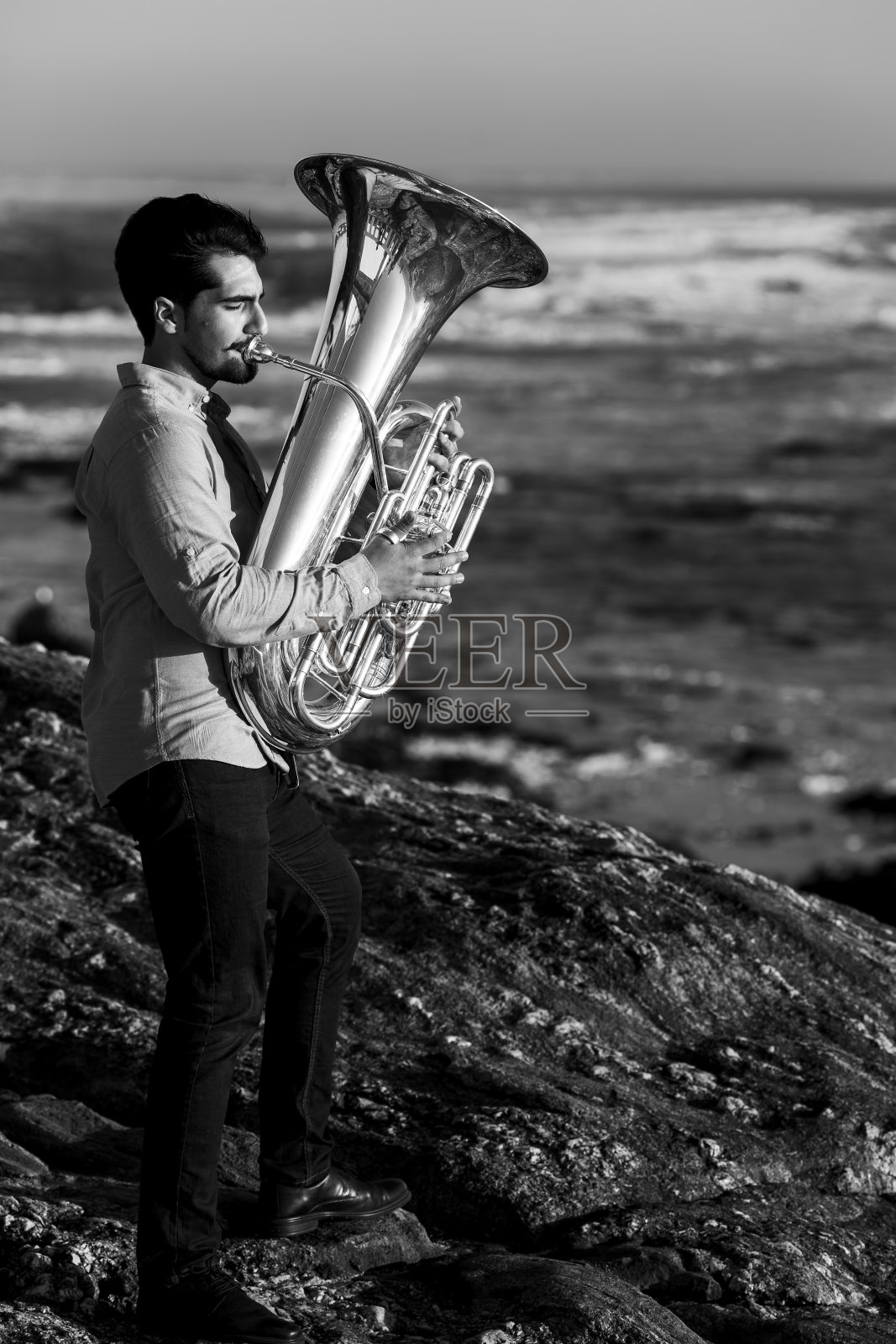 一位男音乐家在海边吹奏大号。黑白照片。照片摄影图片