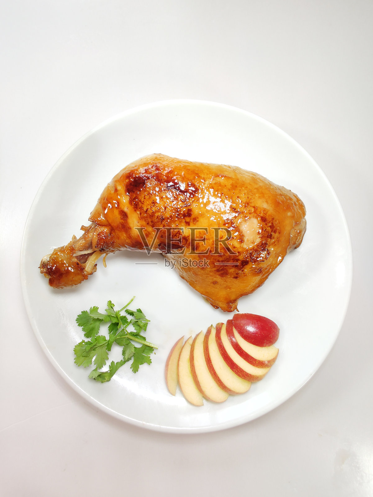 特写的烤鸡腿和苹果片在一个白色盘子，俯视图照片摄影图片