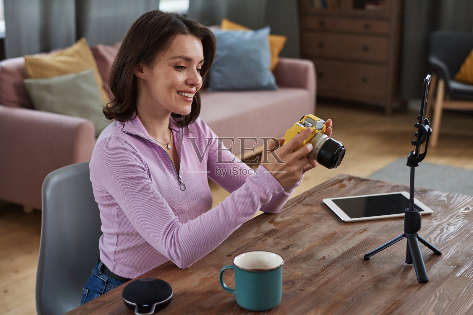 积极有吸引力的年轻白人摄影师坐在桌子上，用三脚架上的智能手机，在准备现场拍摄的时候浏览相机照片照片摄影图片