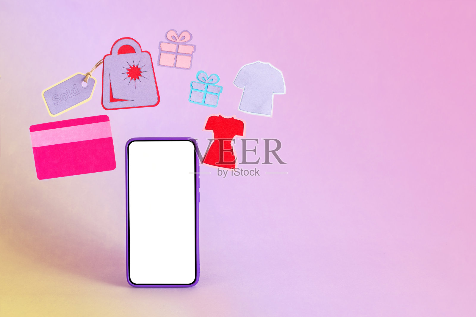 紫色背景上被信用卡、购物袋、衣服和礼物包围的智能手机照片摄影图片