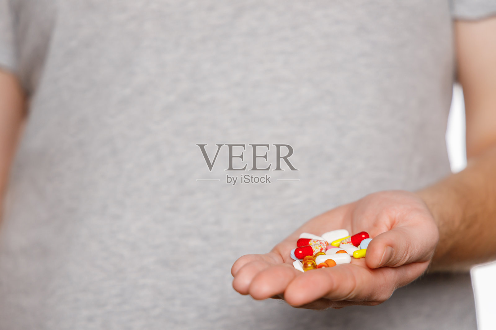 穿着灰色t恤的男人手里拿着一堆五颜六色的药丸。照片摄影图片