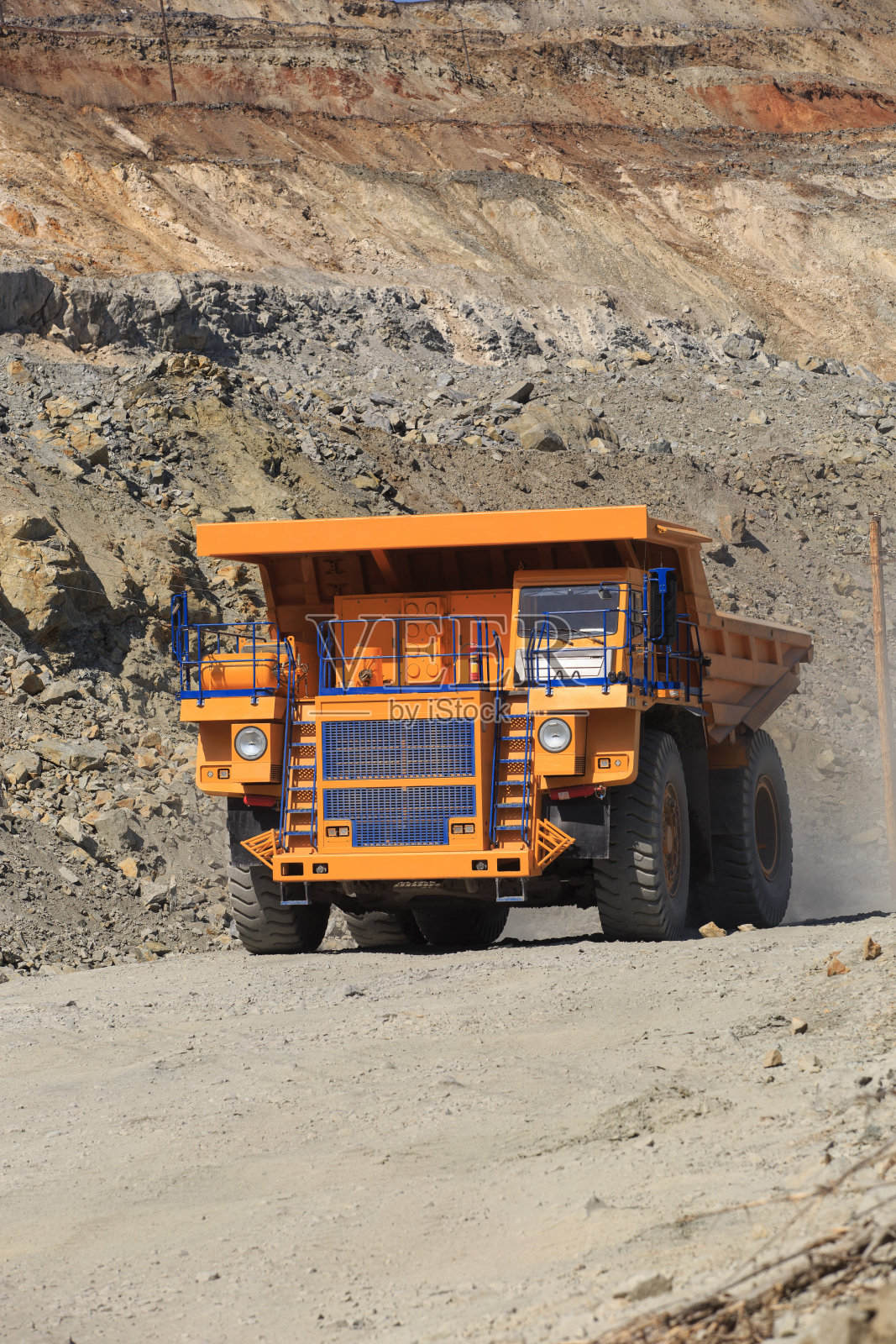 在一个阳光明媚的日子里，大型黄色矿用自卸卡车在路上行驶。照片摄影图片