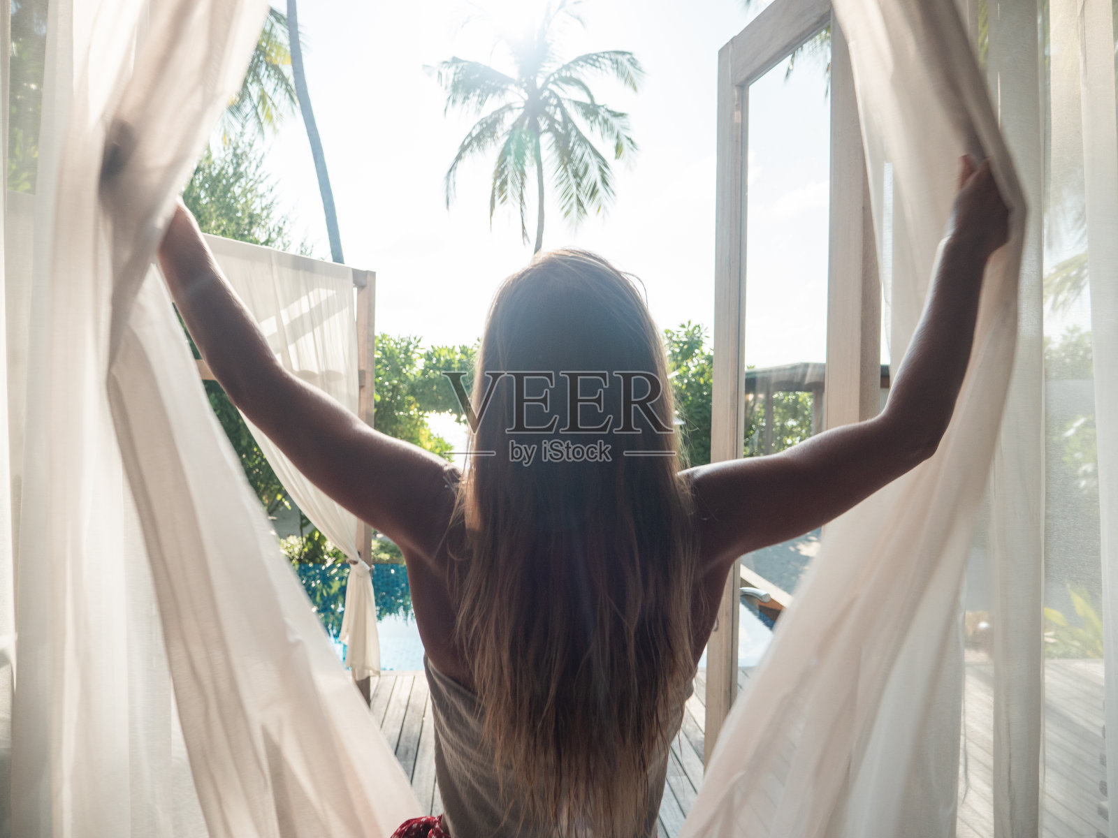 日出时分，一名女子在酒店房间拉开窗帘照片摄影图片
