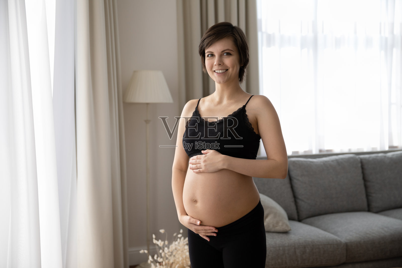 快乐的孕妇穿着黑色内衣抱着大肚子照片摄影图片