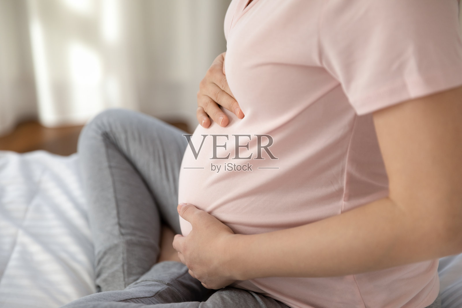 穿着粉色t恤的准妈妈坐在床上照片摄影图片