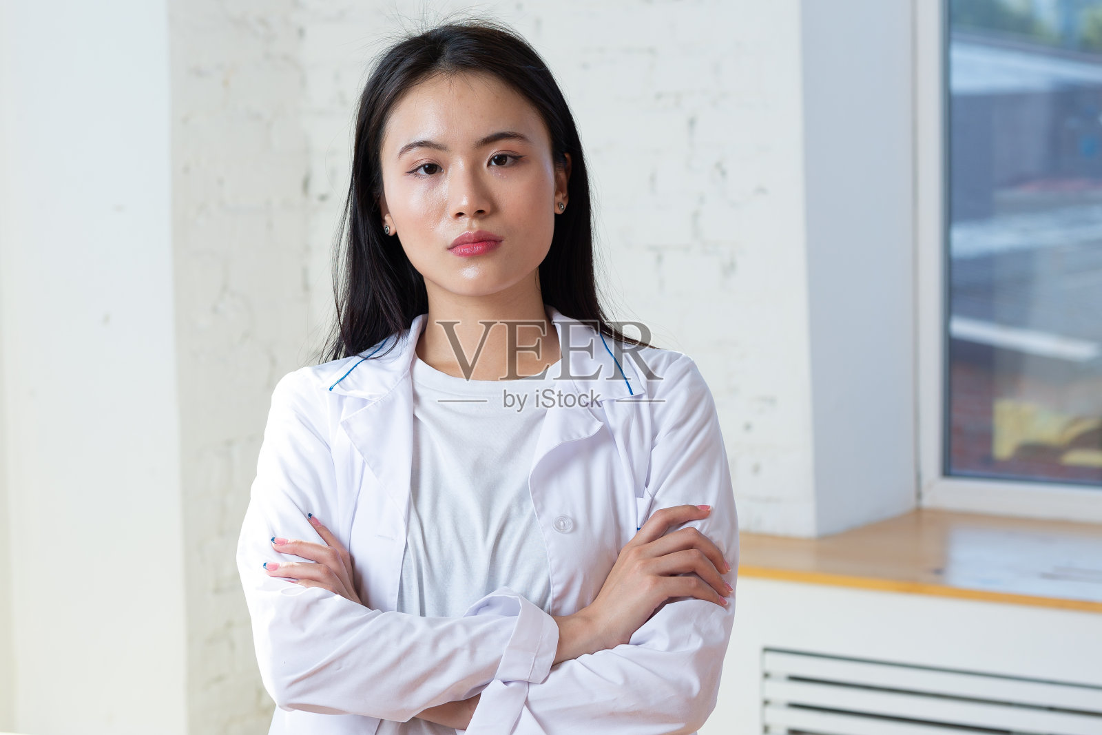 亚洲女医生身穿白色医用大褂，手持听诊器，背景为粉红色照片摄影图片