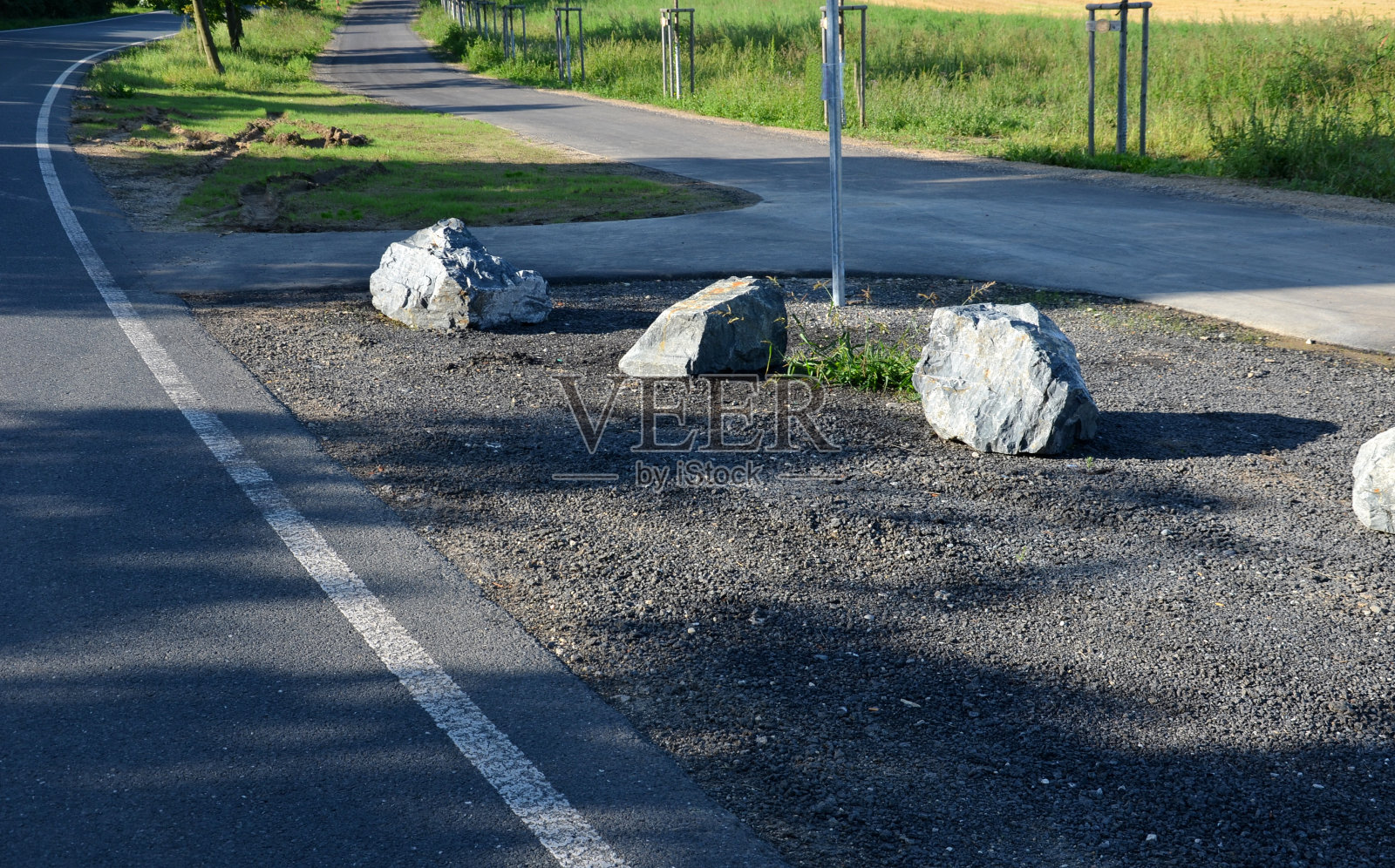 车道之间用灰色的石头来防止停车。乡村公路和自行车道旁的停车场交通解决方案。沥青路面和草坪照片摄影图片