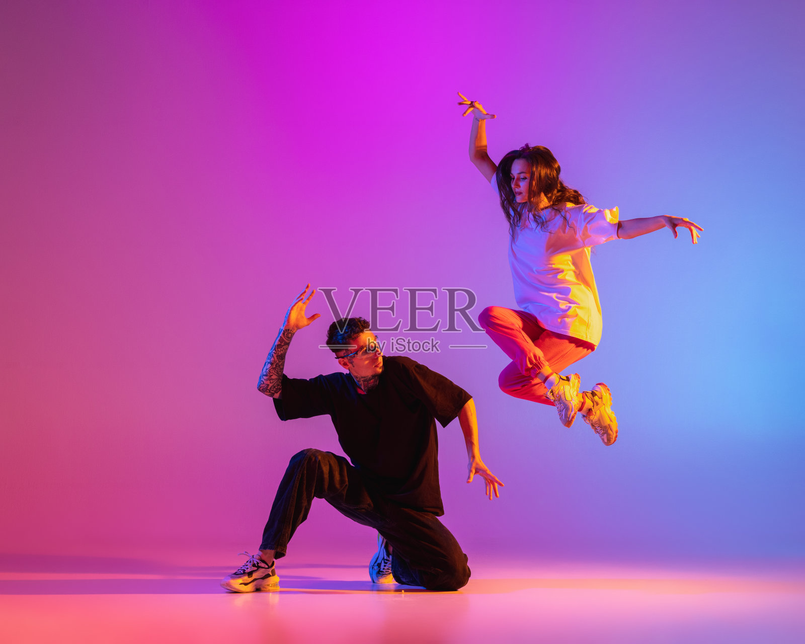 两个年轻人，一男一女，穿着休闲装，在霓虹灯下的粉色背景下跳着现代舞、嘻哈舞。照片摄影图片